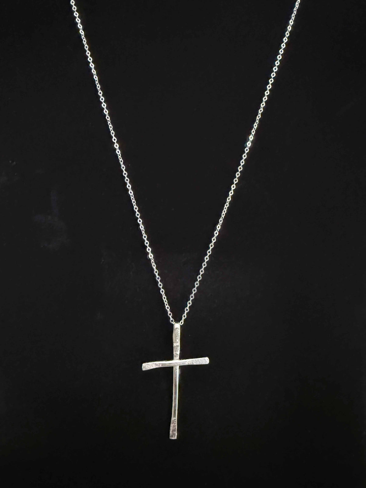 Handcrafted sterling silver cross necklace on a black background, full view